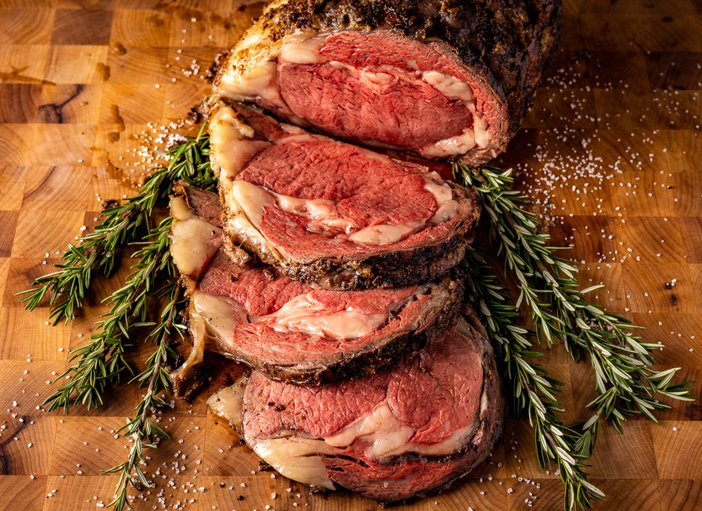 Sliced prime rib roast on a bed of fresh herbs.