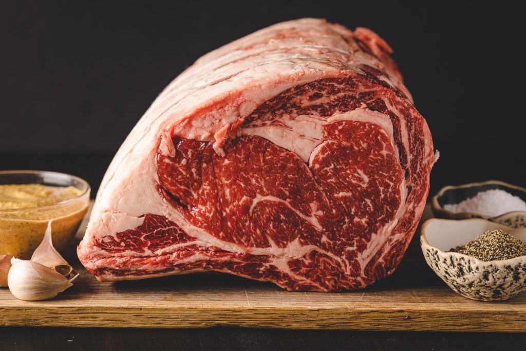 Uncooked prime rib on a cutting board next to bowls of spices.