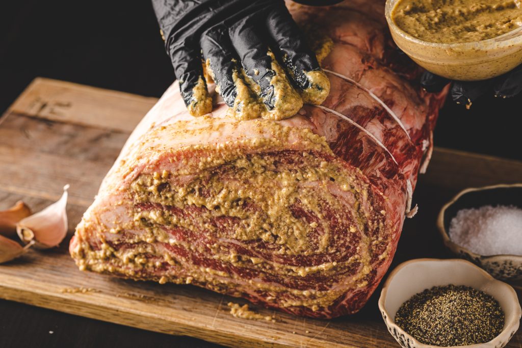 Prime rib being slathered with a horseradish mustard sauce.
