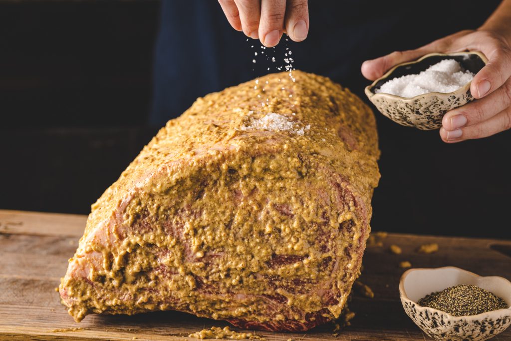 Salt being sprinkled on a prime rib roast.